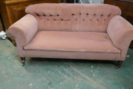 A two seater Chesterfield sofa raised on turned front supports and brass castors, stamped, 180cm
