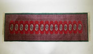 A Persian red ground wool runner with Bokhara style design and emerald green borders, 64 x 188cm