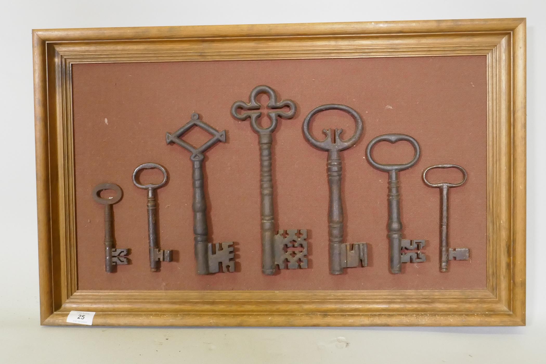 A collection of seven antique keys, mounted on a pine frame, largest key 28cm long