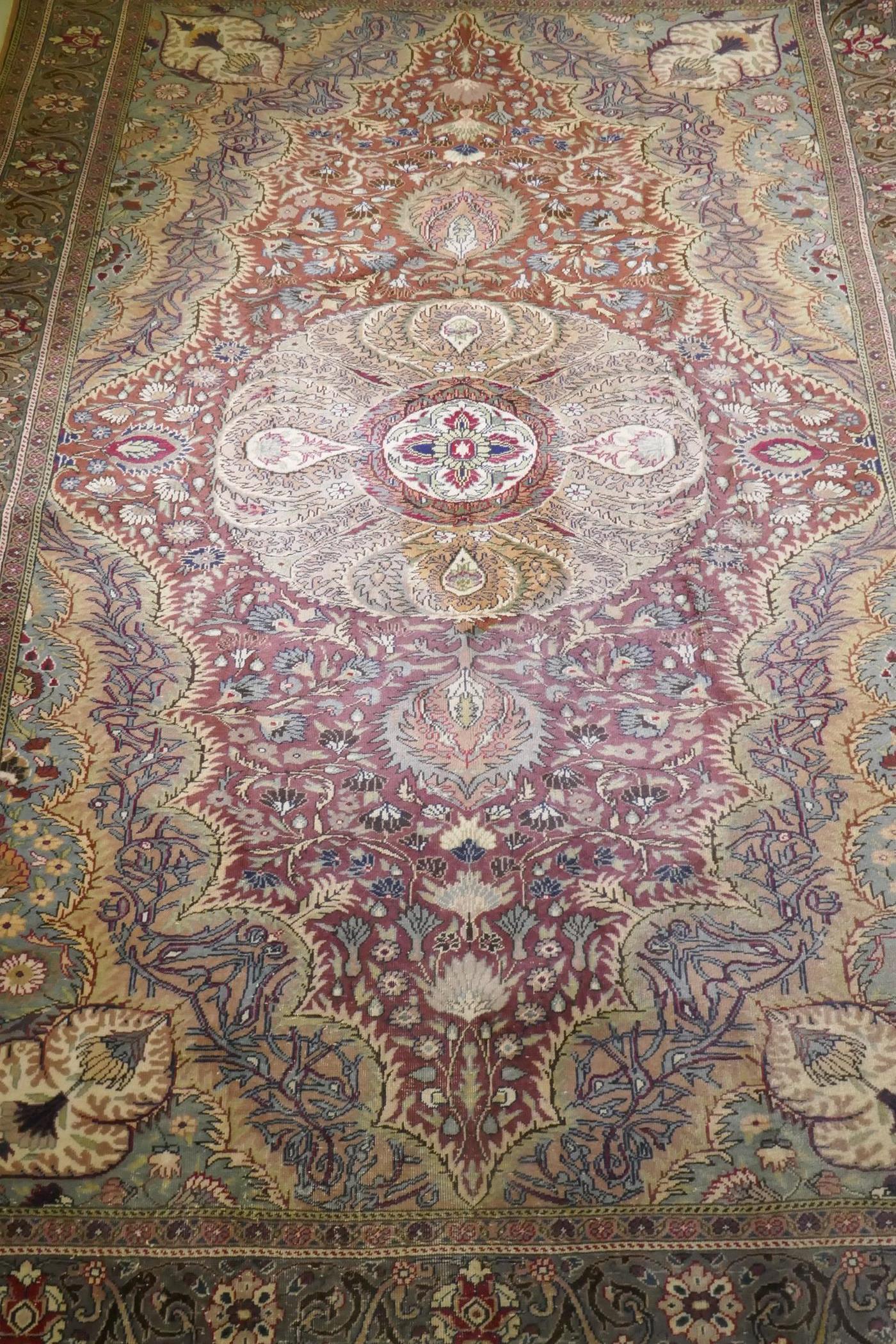 A Turkish Hereke wool carpet with central design on a faded terracotta field, with blue/grey