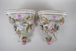 A pair of Dresden style porcelain wall brackets decorated with putti and flowers, 24cm high