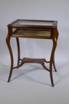 A mahogany bijouterie cabinet with shaped top, raised on splay supports united by an under tier,