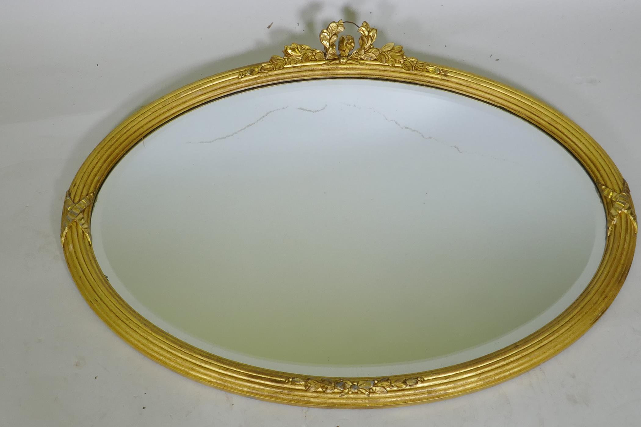 A gilt oval mirror with bevelled glass, AF losses, 82 x 60cm