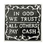 Cast iron 'In God we Trust' sign with white writing on a black ground