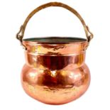 A large copper cauldron with brass mounts and handle.