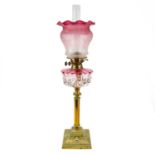 A Victorian brass oil lamp with a glass oil reservoir and cranberry shade.