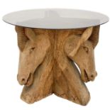 A glass top table with a carved wood pedestal in the form of three horses' heads.