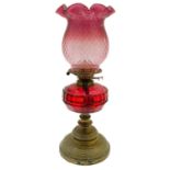 A Victorian brass oil lamp with a cranberry glass shade.