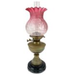 A Victorian brass oil lamp with cranberry etched glass shade.