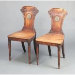 A pair of Georgian mahogany hall chairs with painted armorial to the back, solid seats, raised on