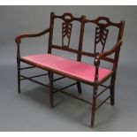 An Edwardian pierced mahogany double chair back settee with upholstered seat raised on turned