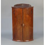 A Georgian mahogany bow front hanging corner cabinet with raised back, fitted shelves enclosed by