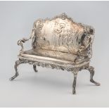 A Continental repousse silver miniature model of a sofa, raised on cabriole legs decorated with