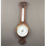 An Edwardian aneroid barometer and thermometer with porcelain dial contained in a carved oak case