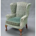 A Georgian style winged armchair upholstered in green material, raised on cabriole, ball and claw