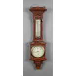 An Edwardian aneroid barometer and thermometer with silvered dial, contained in a carved walnut case