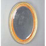 A 19th Century style oval bevelled plate wall mirror contained in a gilt and walnut finished frame