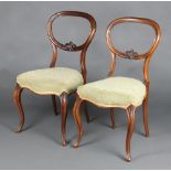 A pair of Victorian carved walnut balloon back dining chairs with carved mid rails and over