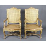 A pair of 19th Century French gilt painted open arm salon chairs with woven cane seats and backs,