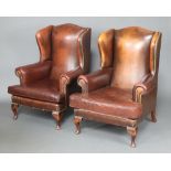 A pair of Georgian style wing armchairs upholstered in brown leather, raised on cabriole supports
