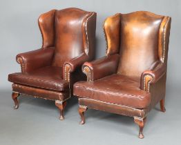 A pair of Georgian style wing armchairs upholstered in brown leather, raised on cabriole supports