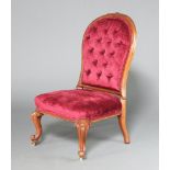 A Victorian carved mahogany show frame nursing chair upholstered in red buttoned material, raised on