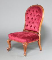 A Victorian carved mahogany show frame nursing chair upholstered in red buttoned material, raised on