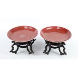 A matched pair of early 20th Century Chinese copper red shallow dishes on wooden stands 14.5cm