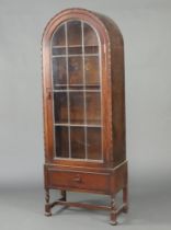 A 1930's oak arch shaped display cabinet, fitted shelves enclosed by a lead glazed panelled door,