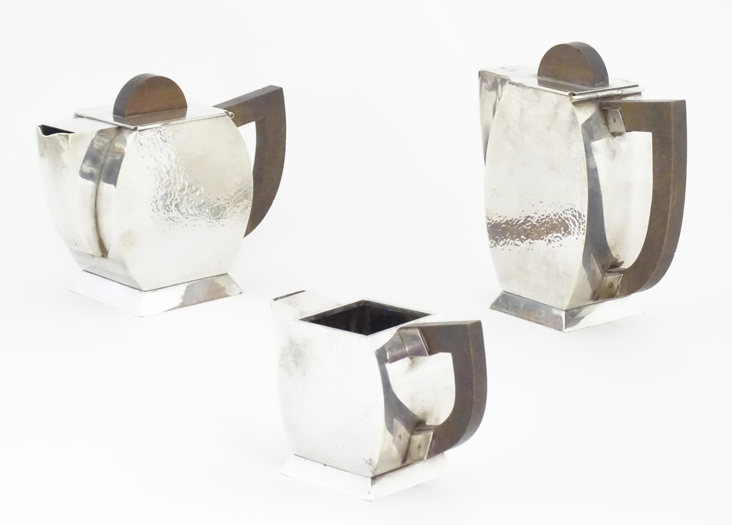 An Art Deco three piece silver plate tea set with hammered decoration and wooden handles, comprising
