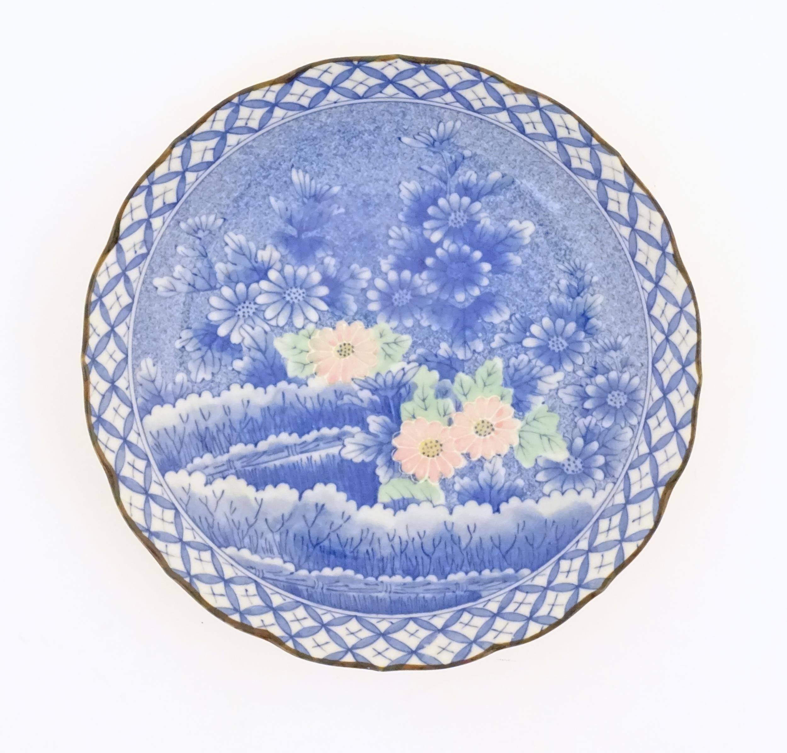 An Oriental blue and white plate with pink and green highlights depicting flowers. Character marks