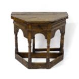 A Victorian oak credence table with a canted hinged table top above a carved frieze and short