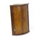 A George III oak bow fronted corner cupboard with crossbanded decoration and H - bracket hinges. 27"