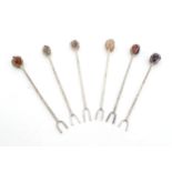 Six white metal cocktail sticks / forks each surmounted with a polished hardstone. Approx. 4 1/2"