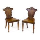 A pair of early / mid 19thC oak hall chairs with armorial shaped backrests decorated with carved