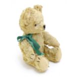 Toy: A 20thC plush teddy bear with stitched nose, mouth and claws, pad paws and a green ribbon.