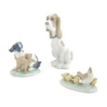 Three Nao models of animals comprising a Basset Hound, a dog and cat 'In Harmony', and a chicken