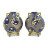 Two Royal Worcester Aesthetic Movement moon flask vases with twin gilt handles and raised feet,
