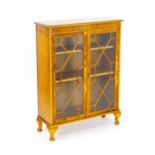 A yew wood veneered astragal glazed cabinet with a moulded top and two doors and raised on four