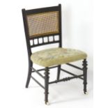 A 19thC ebonised side chair / nursing chair with a caned backrest above a floral upholstered seat