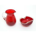 Two items of glassware comprising a red glass water jug with clear glass handle, and a red glass