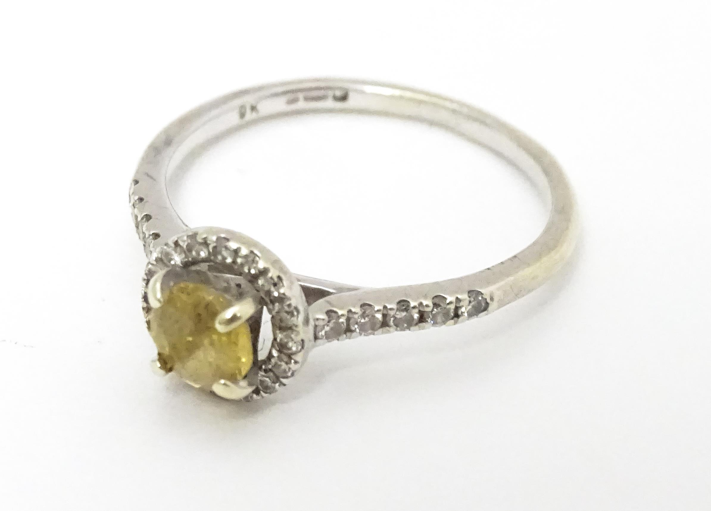 A 9ct white gold ring set with central citrine coloured stone bordered by diamonds and with