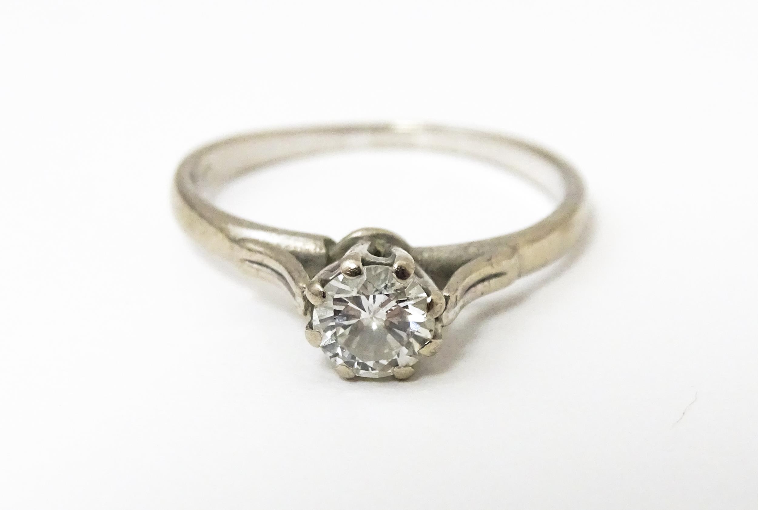 A white metal ring set with central diamond solitaire. Diamond approx. 1/8" diameter Ring size