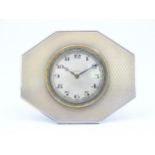 An easel back clock with white metal surround having engine turned decoration detail. The dial