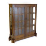 An early 20thC oak Arts & Crafts bookcase with a moulded cornice above glazed, panelled sides and