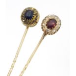 Two yellow metal stick pins, one surmounted by a central sapphire bordered by diamonds, the other