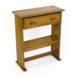 An early 20thC oak Cotswold school side table with carved top above a single short drawer and a book