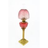 An early 20thC oil table lamp, the cranberry glass shade and reservoir supported by a brass