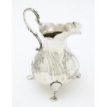 A Victorian silver cream jug with engraved decoration raised on three swept feet, hallmarked