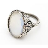 A white metal ring set with central oval moonstone cabochon and with fruiting vine detail to